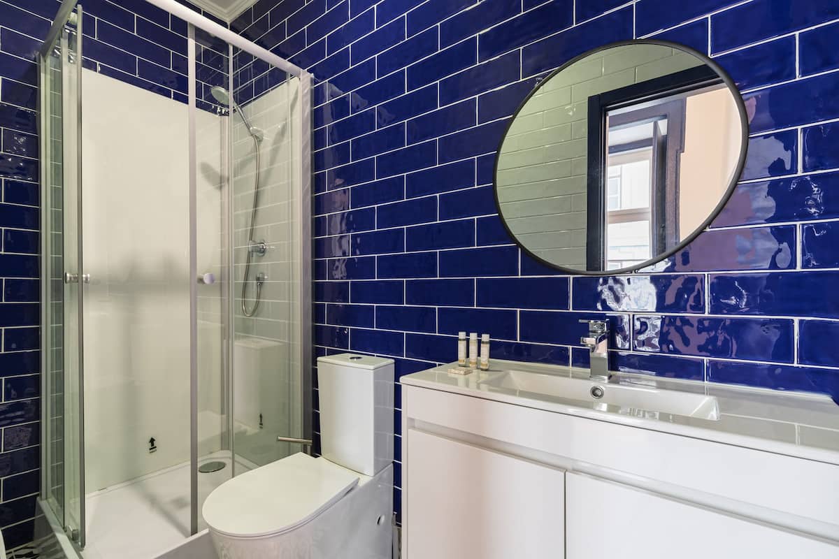 Een badkamer met blauwe betegelde wanden, een douchecabine met glazen wanden, een witte wastafel en een spiegel.