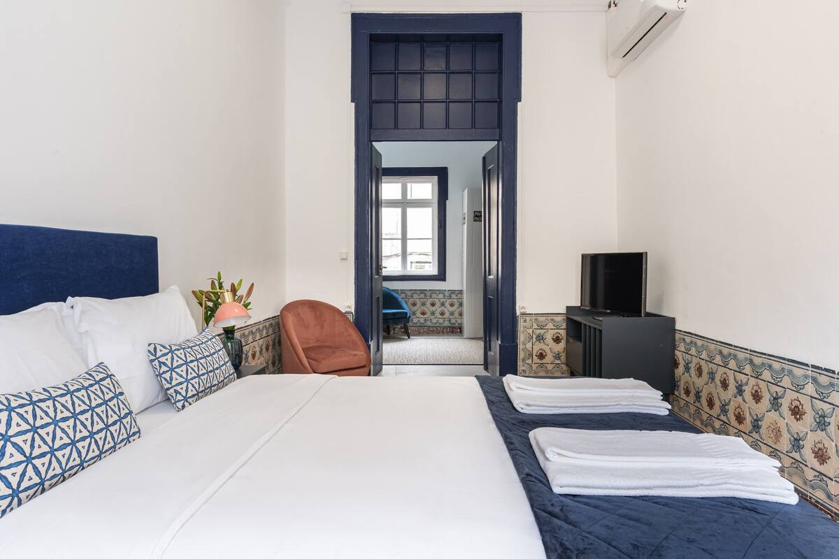 Hotelkamer met een bed, televisie, stoel en een badkamer door een geopende deur zichtbaar.