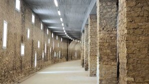 Ein langer Korridor mit Steinwänden und einer Beton Decke, der gleichmäßig verteilte Fenster und einen glatten Boden aufweist.