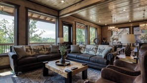 Un salón amplio con ventanas grandes, techo de madera y muebles de cuero.