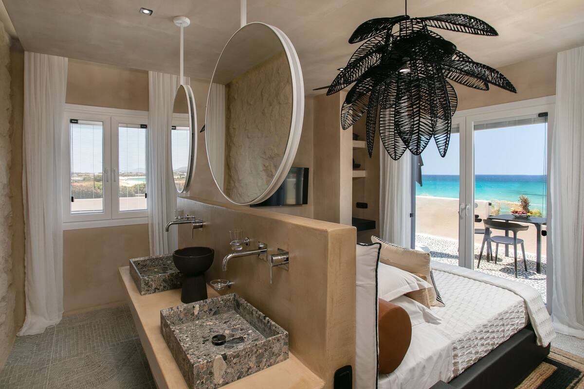A modern hotel room with a large bed, a bathroom with a granite sink, and a view of the beach.