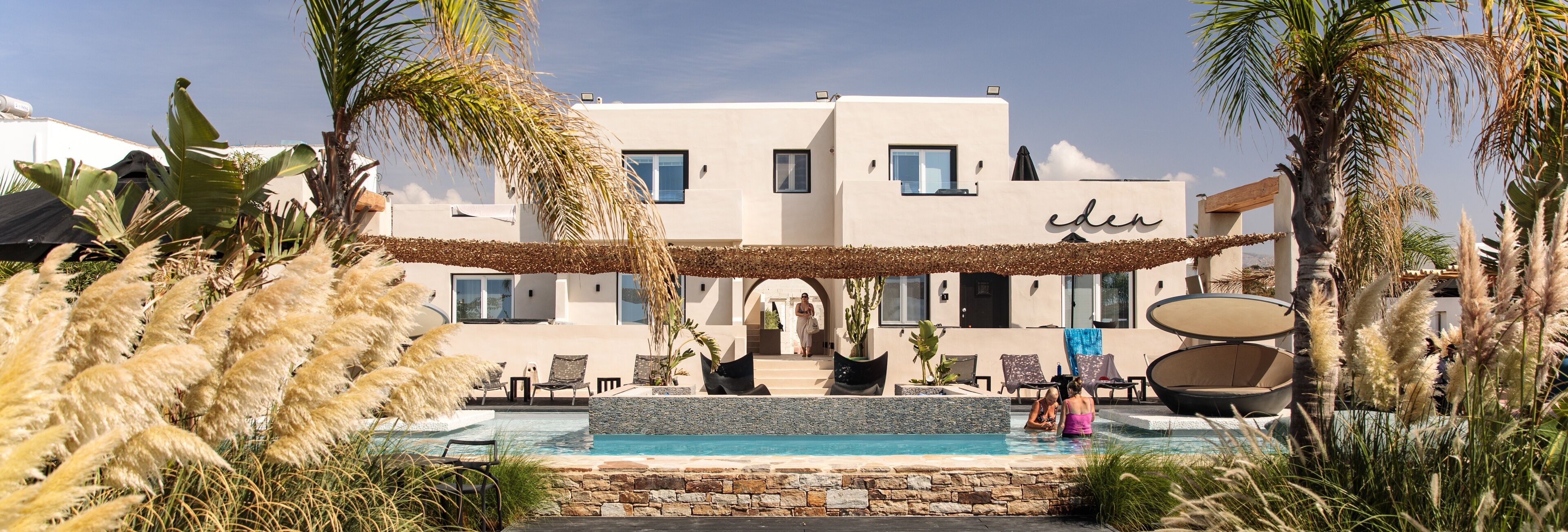 Un hotel moderno con piscina, sillas de descanso y plantas tropicales.