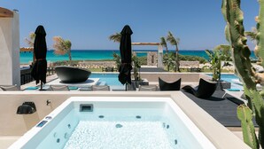 Zona de piscina con hidromasaje, sillones de descanso, sombrillas y vista al océano.