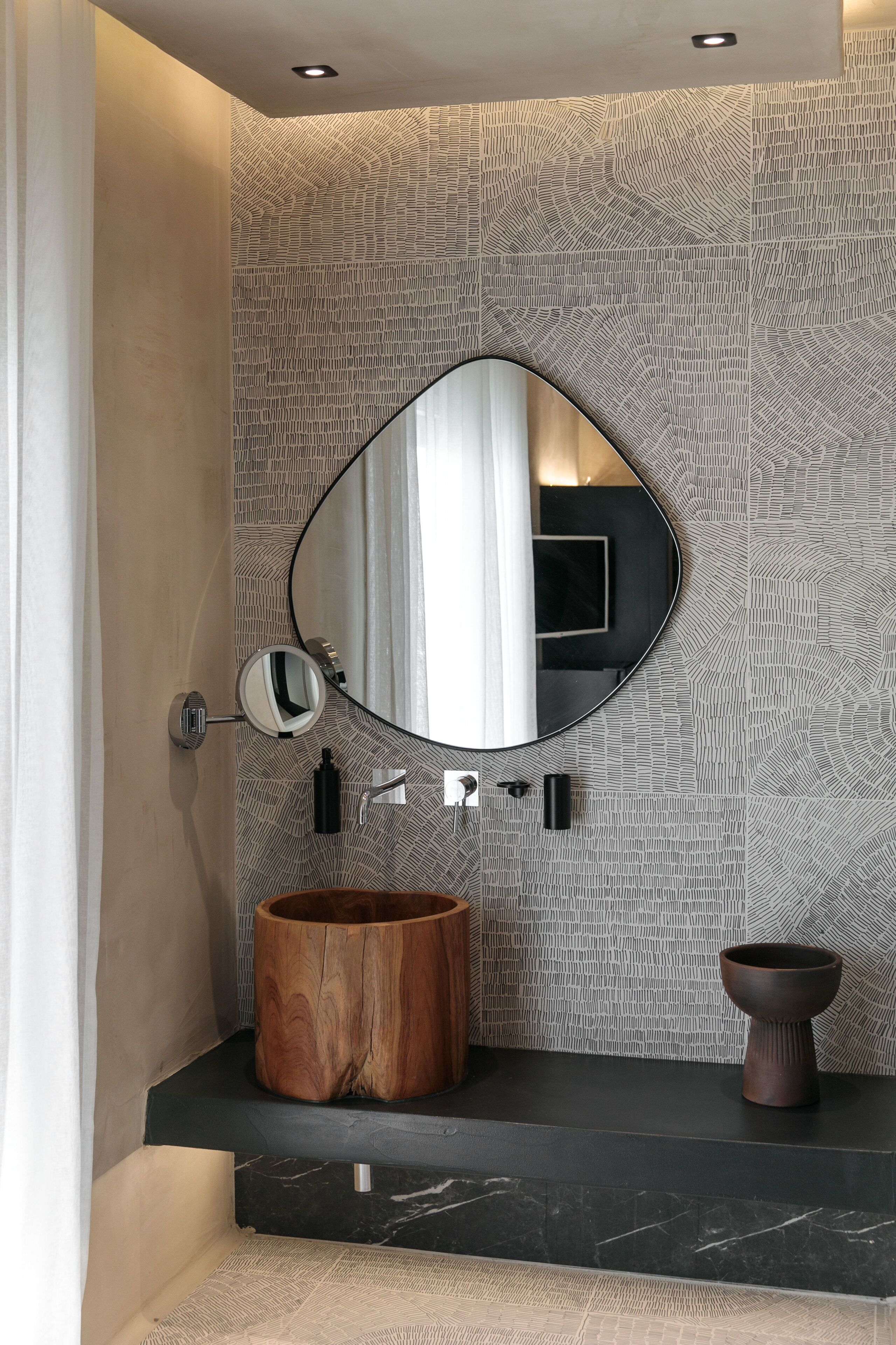 A bathroom with a round mirror, wooden basin, and a patterned wall.
