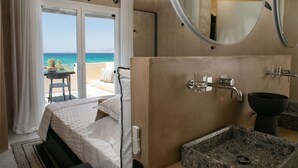 Habitación de hotel con cama, baño con lavamanos y espejo, y vista al océano.