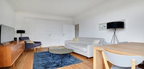 A modern living room with a sofa, a coffee table, a TV, and a dining table.