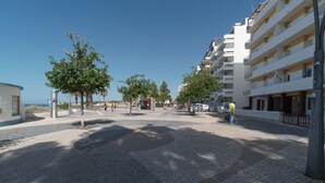 Una piazza pavimentata con alberi, una piccola edicola e una fila di edifici a più piani con balconi.