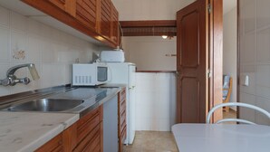 Una cucina compatta con mobili in legno, un piano di lavoro bianco, un lavello, un forno a microonde e un frigorifero.
