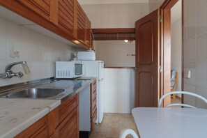 A compact kitchen with wooden cabinets, a white countertop, a sink, a microwave, and a refrigerator. - Viggo Red Apartment, Armacao de Pera, Algarve (Armação de Pêra)