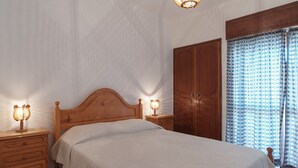 Camera da letto con un letto in legno, due comodini con lampade, un armadio e una finestra con tende a motivi.