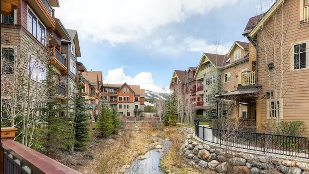 A residential area with multi-story buildings, a stream, and a mountainous backdrop. - Centrally located ski chalet with shared hot tub and pool - right in downtown (Breckenridge)