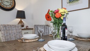 A dining table set with plates, cutlery, and wine glasses, surrounded by wicker chairs and a vase with flowers. - Flat 4 (Newquay)