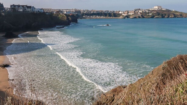 A coastal town with a beach, rocky shoreline, and buildings on a hill. - Flat 4 (Newquay)