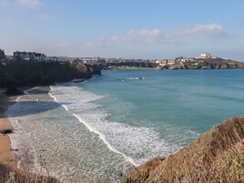 A coastal town with a beach, rocky shoreline, and buildings on a hill.