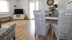 A living room with a TV, wicker chairs, a dining table with wine glasses, and a clock on the wall. - Flat 4 (Newquay)