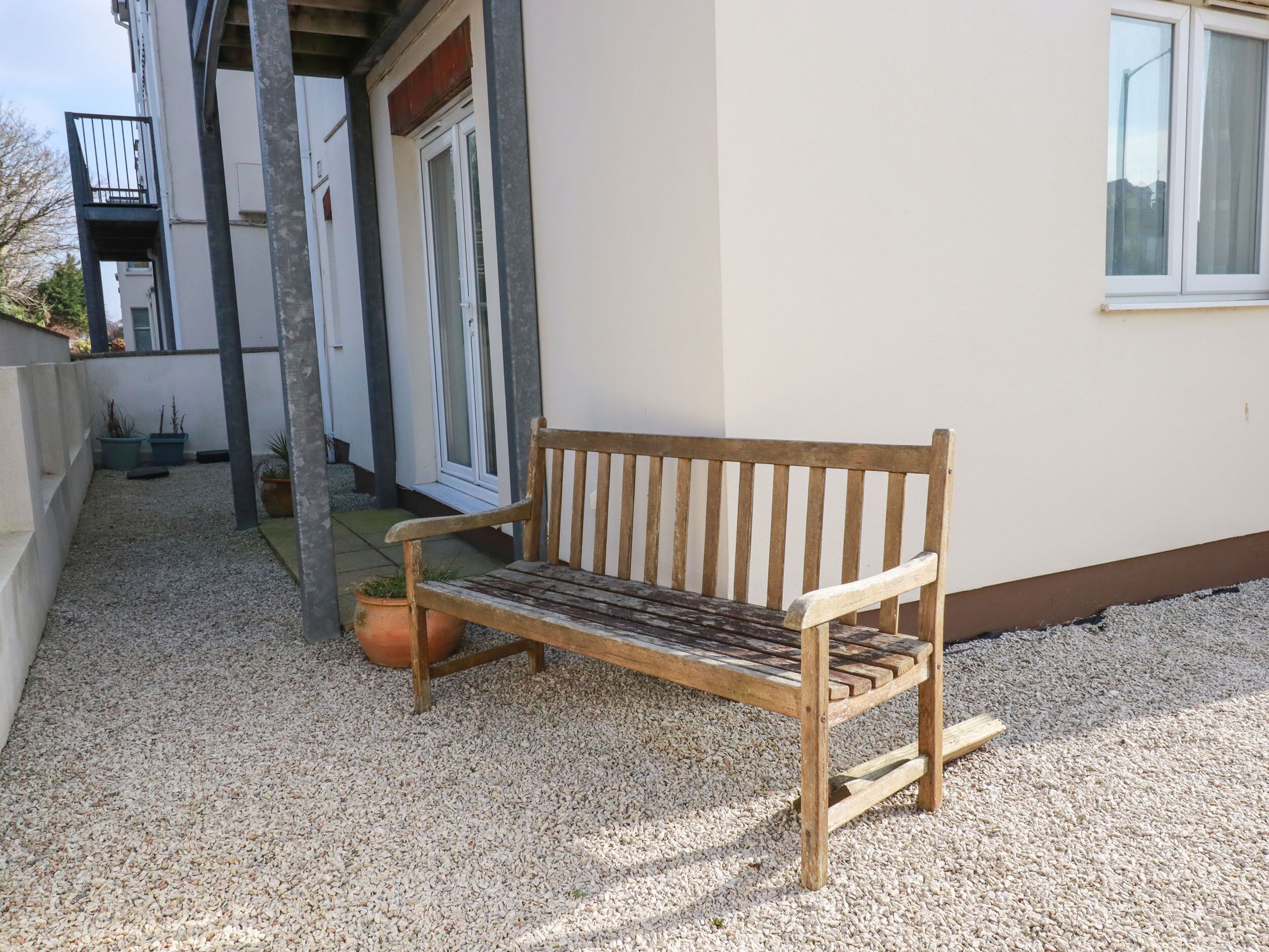 Un banc en bois se trouve à l’extérieur d’un bâtiment, sur un sol recouvert de gravier.