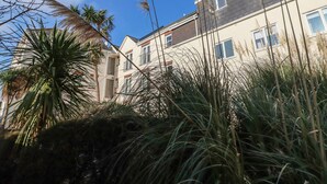 A multi-story building with balconies, surrounded by tall grasses and palm trees. - Flat 4 (Newquay)