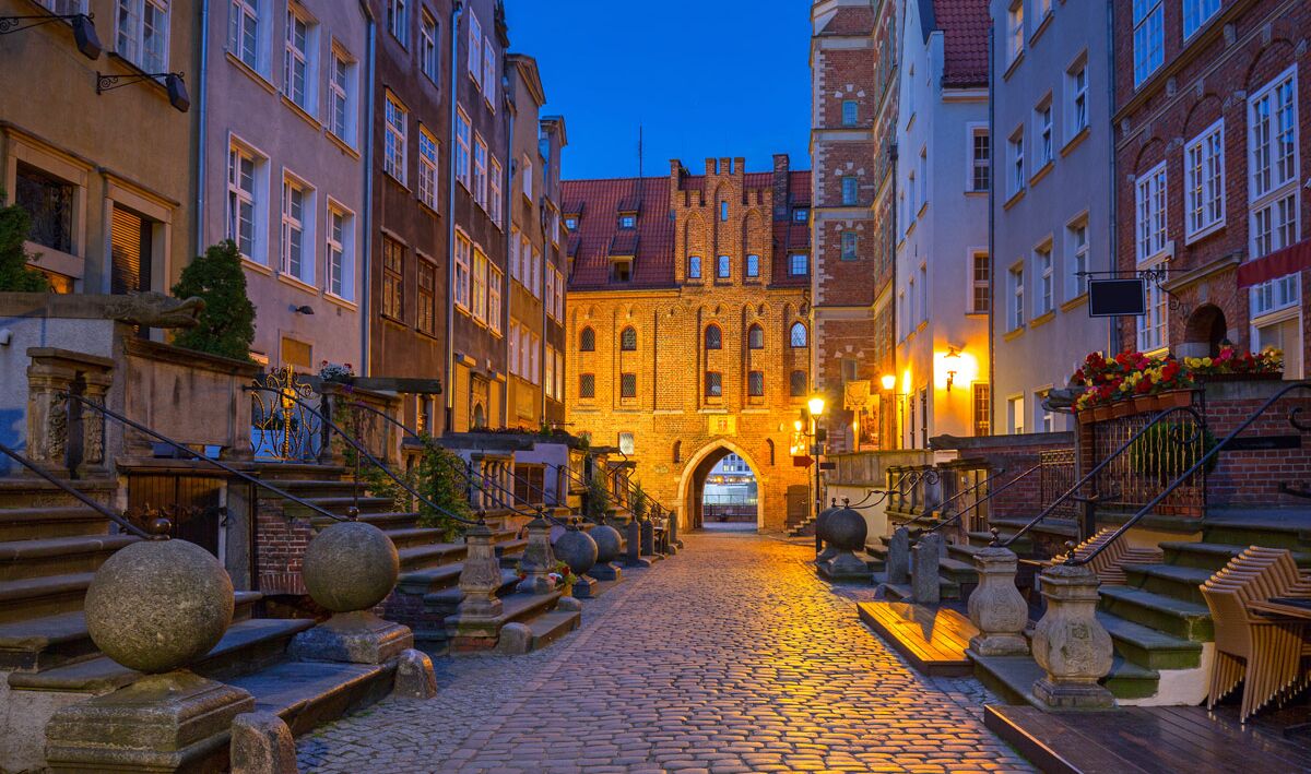 A cobblestone street leading to a historic building with an arched entrance, flanked by traditional European architecture.