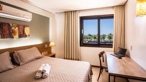 A hotel room with a bed, a desk with a laptop, a window with a view of palm trees, and an air conditioning unit. - Kariri 319A (Caucaia)