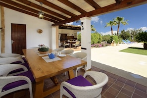 An outdoor patio with a wooden table and wicker chairs, a barbecue area, and a view of the garden. - Teuler Petit for 8 people, magnificent outdoor area, beautiful rural setting (Cas Concos des Cavaller)