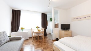 A modern hotel room with a wooden floor, a bed, a sofa, a dining table with chairs, a TV, and a painting on the wall. - Rafael Kaiser - Apartment Cityflow (Graz)