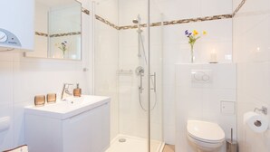 A modern bathroom with a glass-enclosed shower, a white sink with a mirror above it, and a toilet with a roll of toilet paper on the wall. - Rafael Kaiser - Apartment Cityflow (Graz)