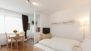 A modern hotel room with a wooden bed, a desk with a chair, a TV, and a dining table with chairs. - Rafael Kaiser - Apartment Cityflow (Graz)