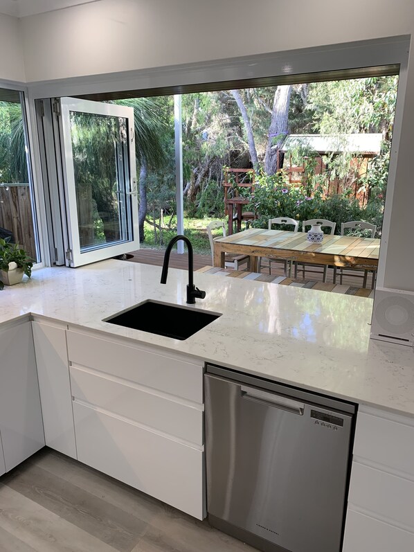 Una cocina moderna con un ventanal grande, muebles blancos y lavavajillas empotrado.