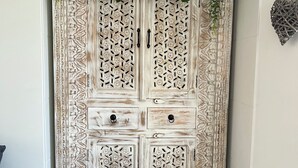 A white, intricately carved wooden wardrobe with two doors and two drawers, featuring a decorative top with hanging plants.