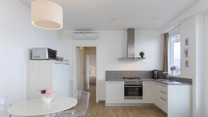 Una cocina moderna con muebles blancos, una estufa a gas y un horno empotrado. Hay un comedor con una mesa y sillas blancas, y un jarrón con flores sobre la mesa.