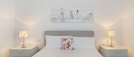 Et pænt og ryddeligt soveværelse med en stor seng, to sengeborde med lamper, en blomstret pude og et maleri på væggen.