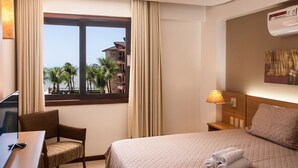 Ein Hotelzimmer mit Bett, Schreibtisch mit Stuhl, Fenster mit Vorhängen, Nachttisch mit Lampe und einer Wandklimaanlage.