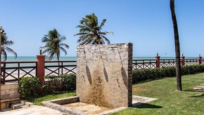 Ein gepflasterter Weg mit einer Steinmauer, Palmen und Blick auf das Meer.