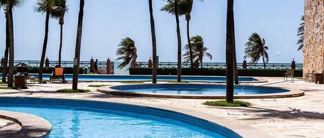 Una piscina rodeada de palmeras, con un cielo azul despejado y vista al mar.