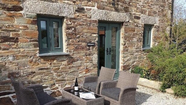 An outdoor seating area with wicker furniture and a table, in front of a stone building with green doors and windows. - Peaceful Rural Retreat, Ideal Base To Explore Cornwall (Wadebridge)