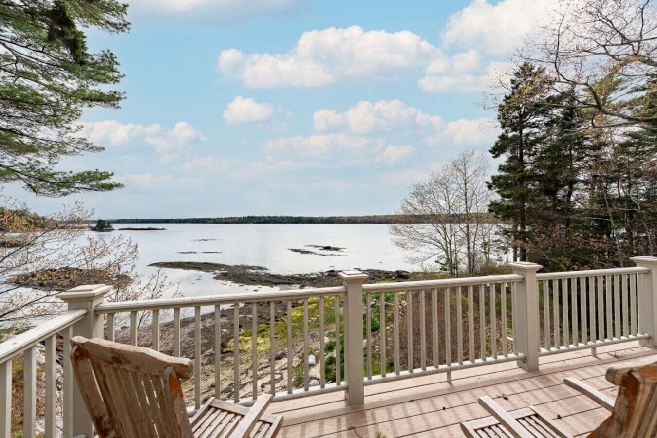 A wooden deck with a railing overlooking a calm lake with visible land in the distance.