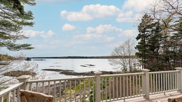 Une terrasse en bois, dotée d’une balustrade, surplombe un lac paisible, et on aperçoit la terre ferme au loin.
