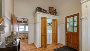 Une pièce spacieuse avec un plancher en bois, une grande porte en bois et une vue sur une buanderie, visible à travers une porte ouverte.
