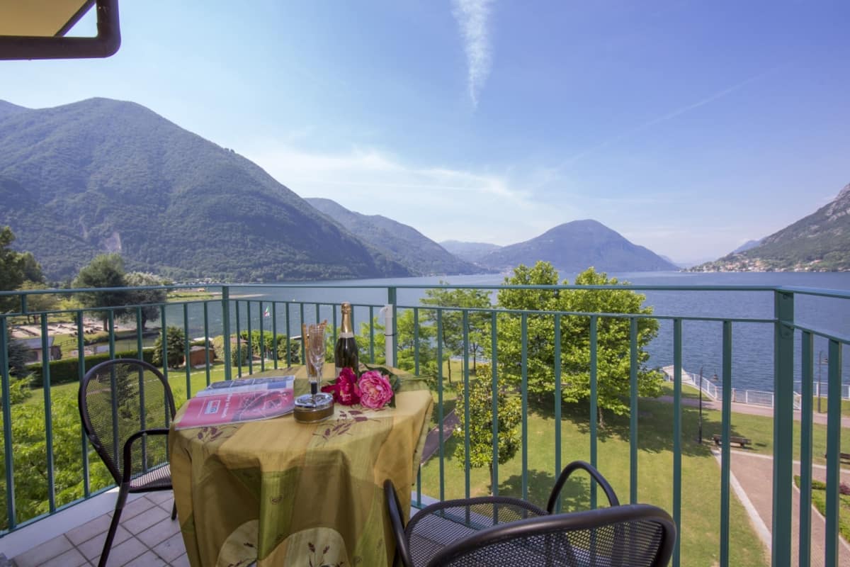 A balcony with a table set for two, overlooking a lake and mountains.
