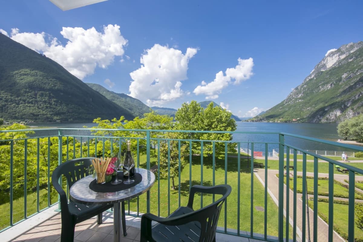 A balcony with a table and chairs overlooking a lake and mountains.