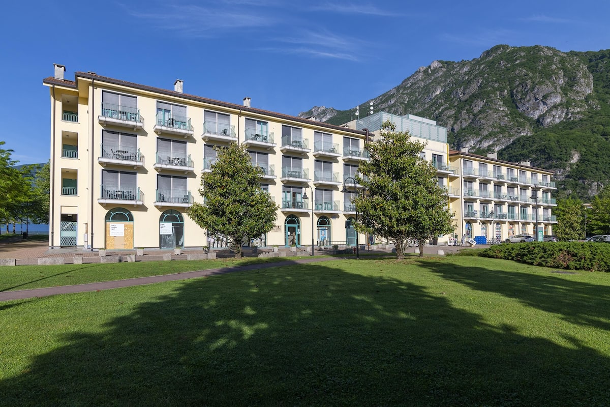 A multi-story hotel with balconies, a mountain backdrop, and a well-maintained lawn.