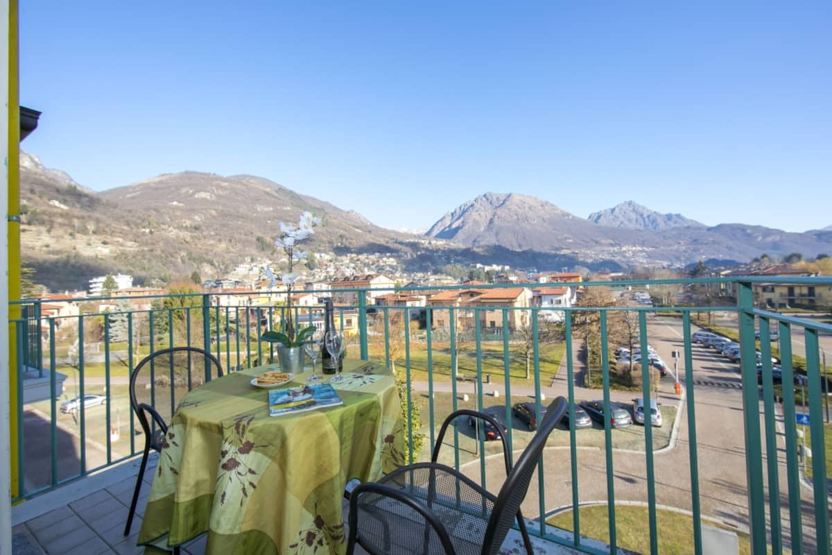A balcony with a table set for dining, overlooking a town and mountains.