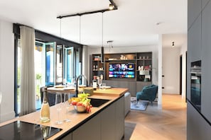 A modern kitchen with a large island, a flat-screen TV, and a dining area with a sofa.