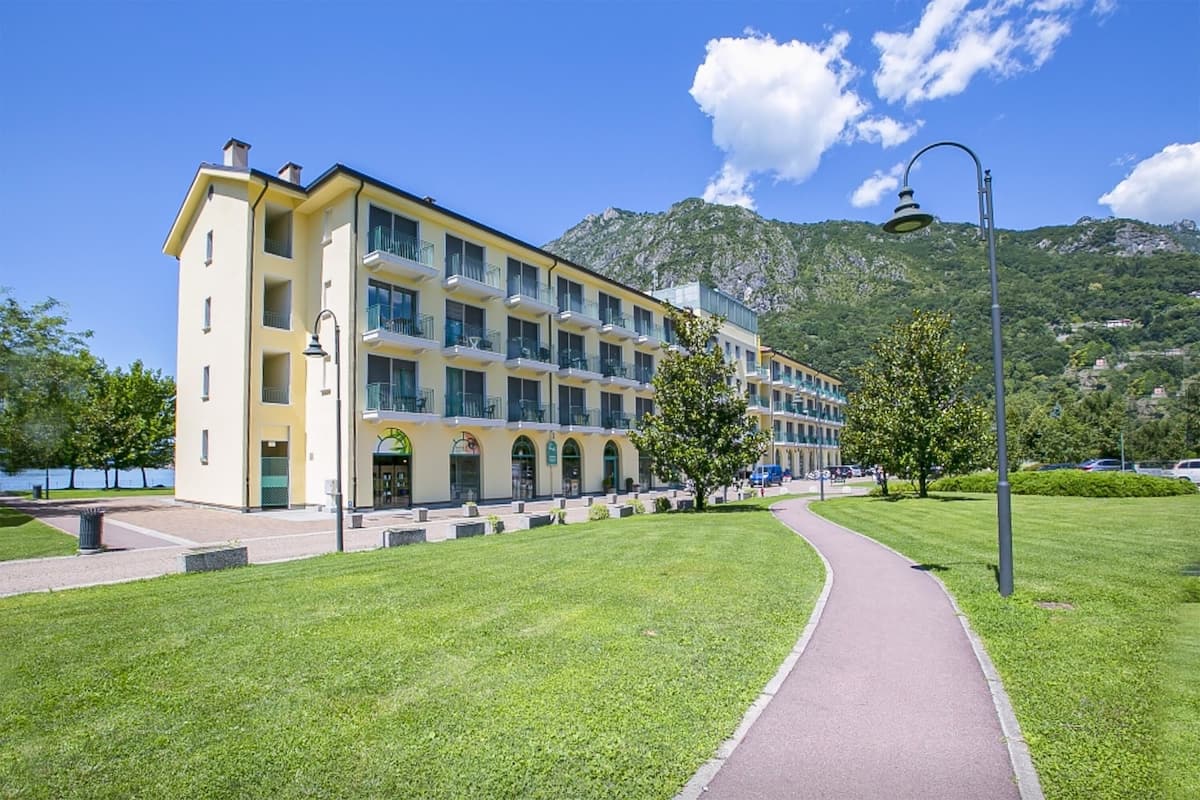 A multi-story hotel with a central courtyard, a paved walkway, and a mountain backdrop.