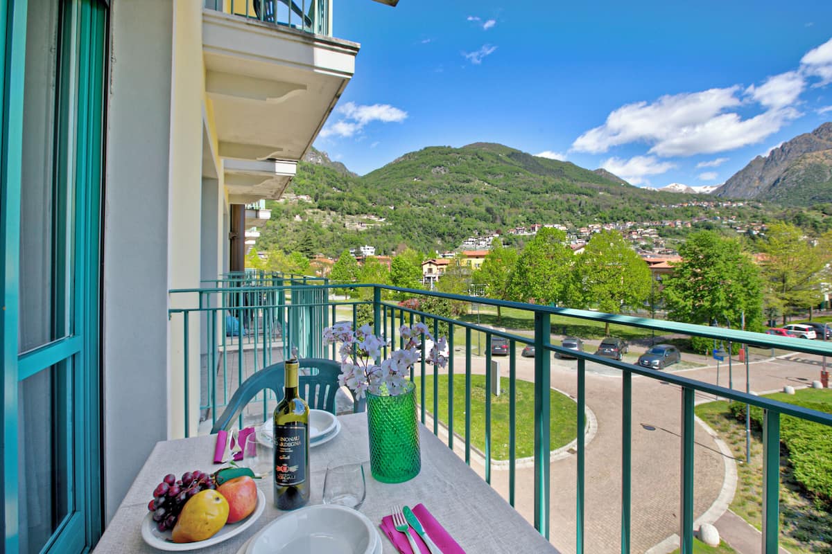 A balcony with a table set for dining, a bottle, and a vase with flowers.