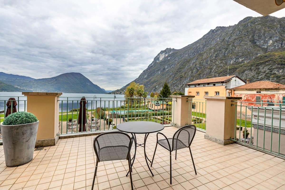 A balcony with a table and chairs, overlooking a lake and mountains.