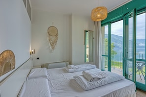 A bedroom with a bed, a dreamcatcher, a hanging light, and a balcony with a view. - Palazzo Apartments - Porto Letizia (Porlezza)