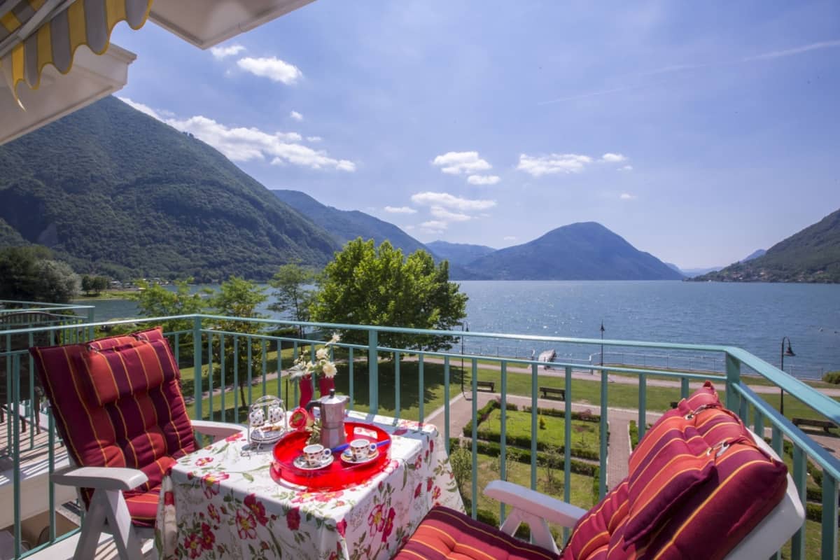 A balcony with a table set for tea, overlooking a lake and mountains.