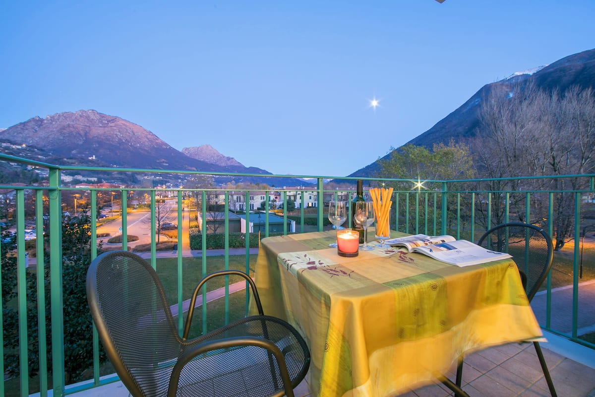 A balcony table with a yellow tablecloth, two chairs, a candle, and a menu.