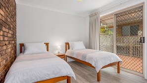 Two beds with white bedding, each with a bedside table and lamp, are positioned in this modern room with a sliding door leading to an outdoor area.